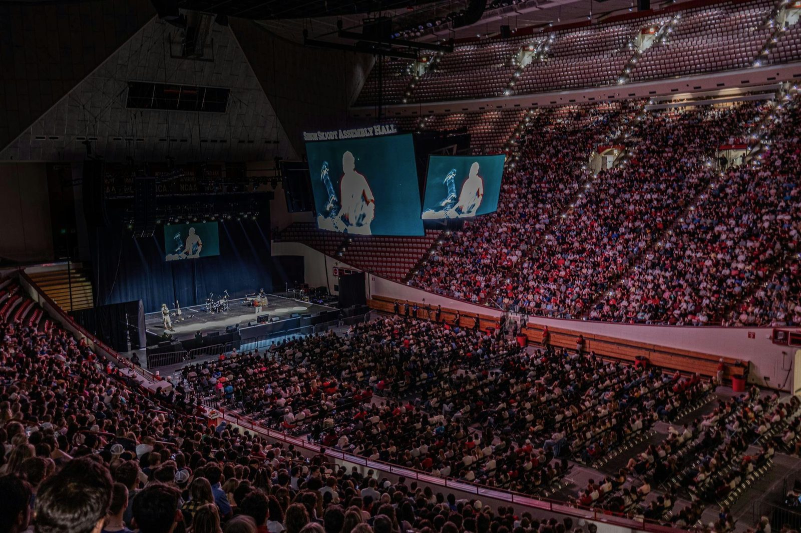 Wide view of the full arena, stage and video walls at left, bowl packed with students