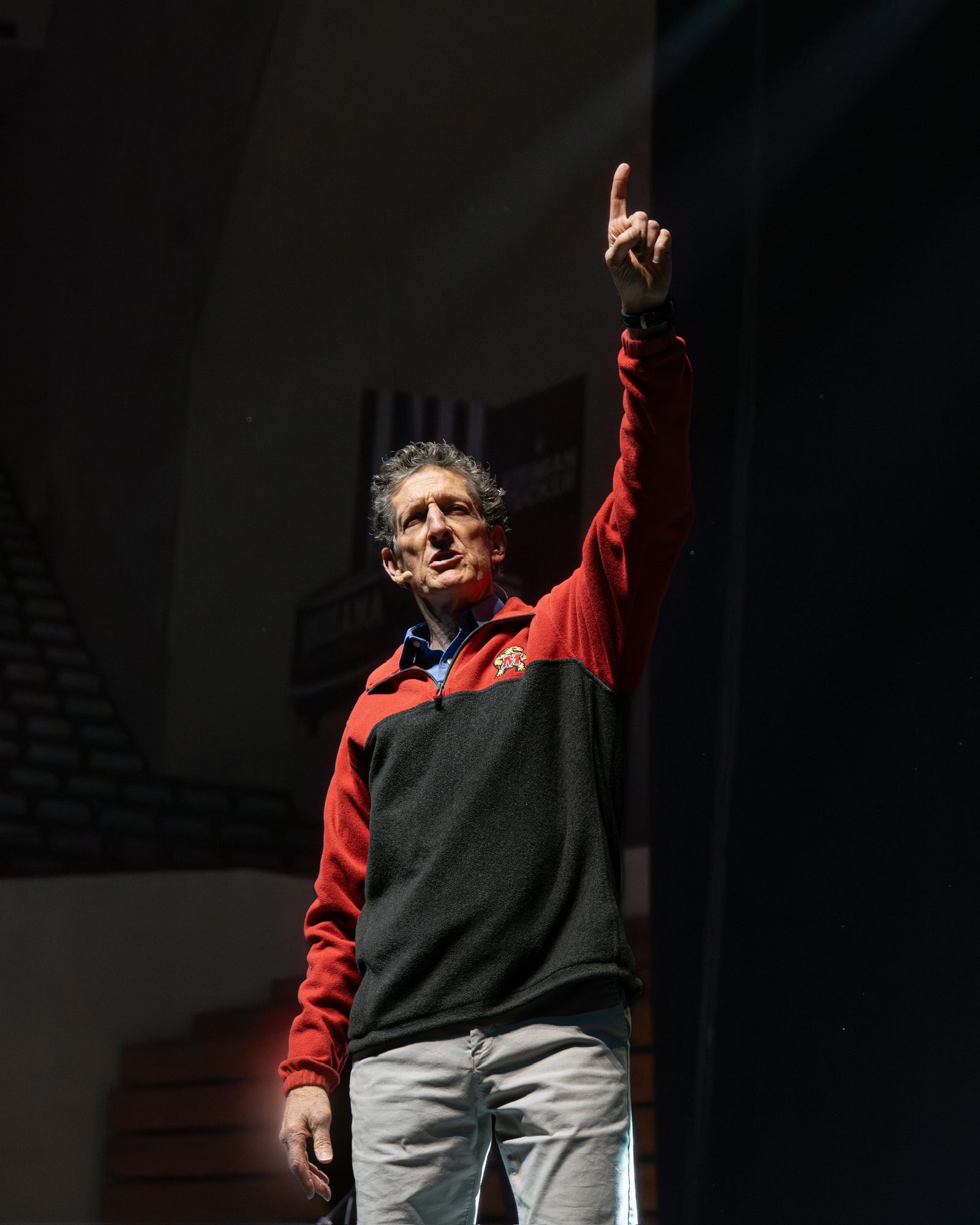 Cliffe Knechtle alone in a spotlight, one finger raised